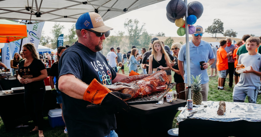 A rib master from the Drinking Team carries a grilled alligator on a tray.